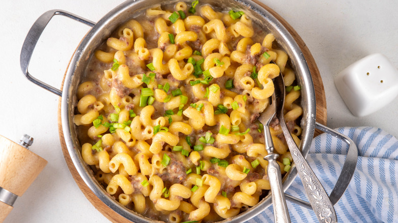 Pot of mac and cheese with crumbled beef, garnished with chopped green onions