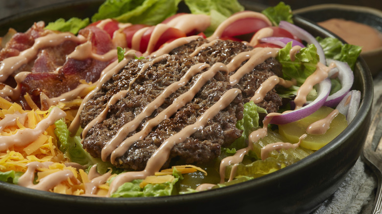 Salad bowl with burger patties, bacon, and drizzle of creamy sauce