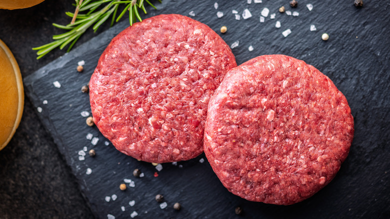 Two raw beef burger patties on black slate