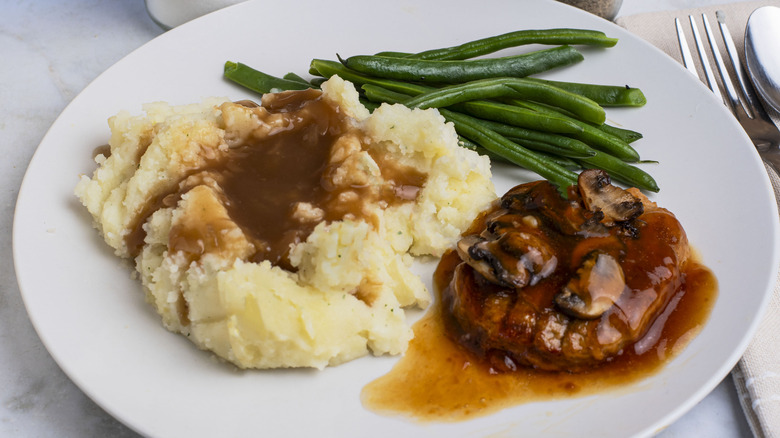 Salisbury steak on plate with mashed potatoes, mushroom gravy, and green beans