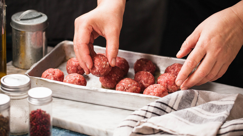 Hands placing meatballs into baking tray