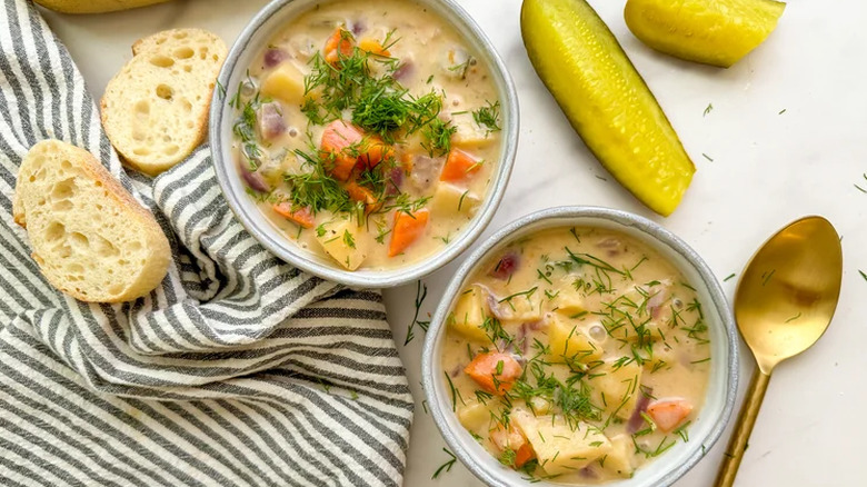 Two bowls of chunky dilll pickle soup with pickles and bread on the side