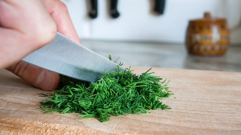 A hand chopping fresh dill on a wooden cutting board