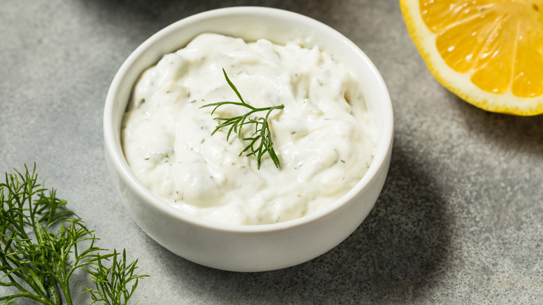 A bowl of dill cream with some dill and a lemon on the side