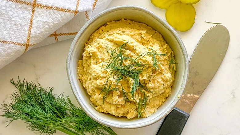 A bowl of hummus with fresh dill and pickles