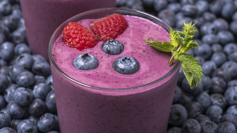 A mixed berry smoothie in a glass with blueberries in the background