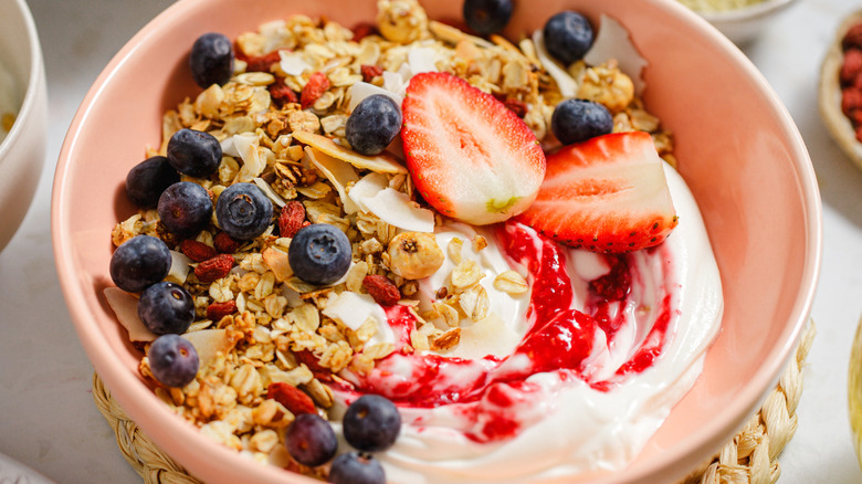 A pink bowl filled with yogurt, granola, and fruit toppings