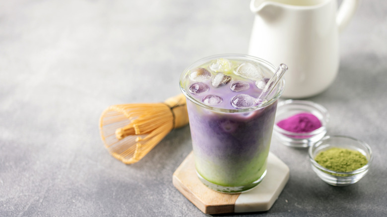 A glass of ube mathca latte with the dry ingredients on the side