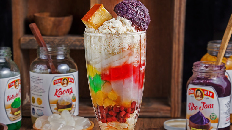 A tall glass of halo-halo dessert with ingredients on the side