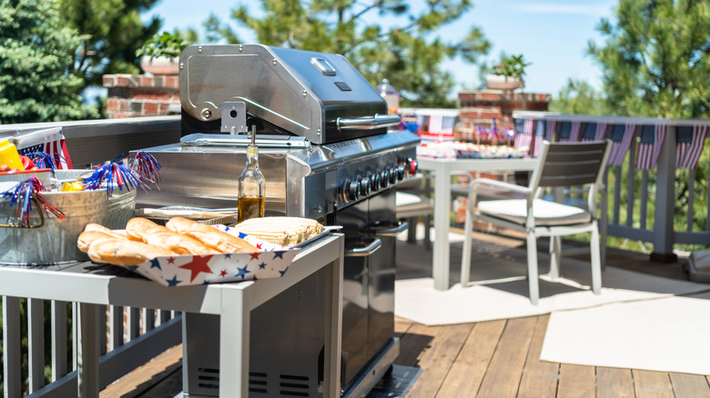 A barbecue on a deck with flag decor, red, white, and blue flair, stainless steel grill, and table with chairs.