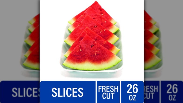 Slices of seedless watermelon quarters stacked in a deli tray.
