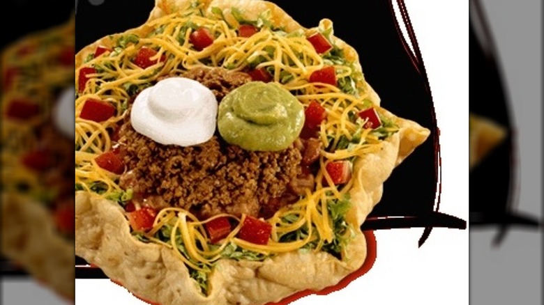 Deluxe taco salad in a crispy tortilla shell bowl against a black and white background