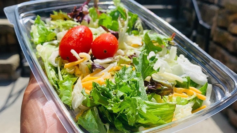 Hand holding Chick-fil-A side salad in clear plastic container