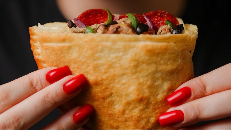 Red-nailed hands holding a supreme Pizza Hut P'zone