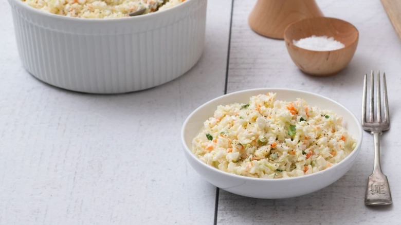 Dish of coleslaw and fork on white table with bigger bowl in background