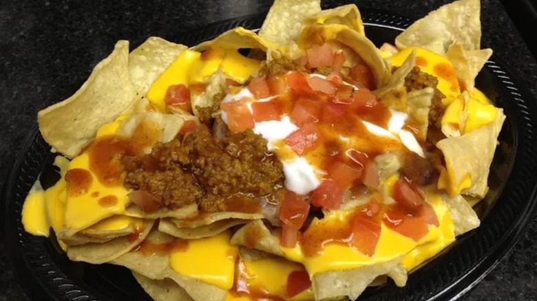 Black plate topped with tortilla chips, cheese sauce, meat, tomatoes, sour cream, and hot sauce.
