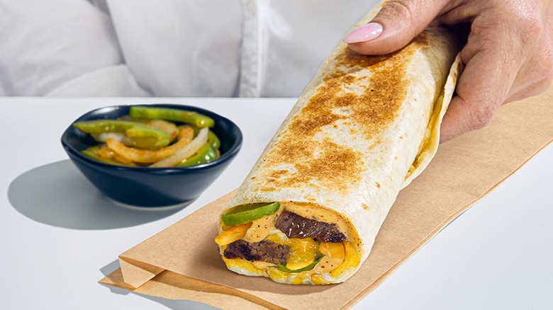 Hand holding Taco Bell fajita rolled quesadilla with fajita veggies on the side