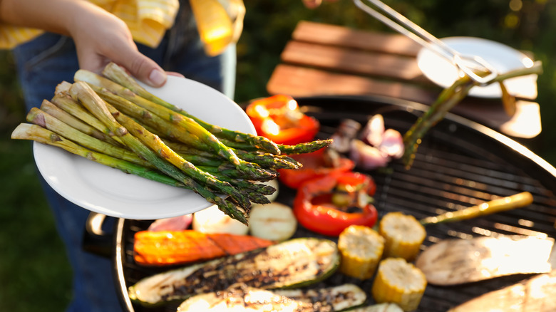 Woman holding vegetables above a grill with grilled vegetables in the background