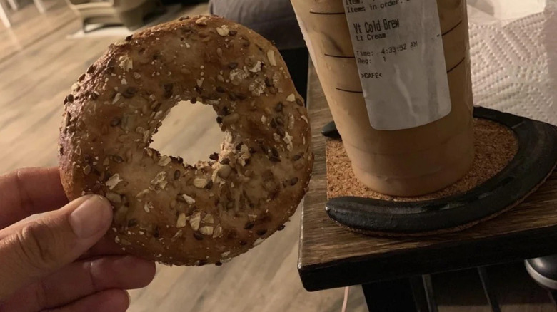 Hand holding a multigrain bagel from Starbucks with an iced coffee in the background