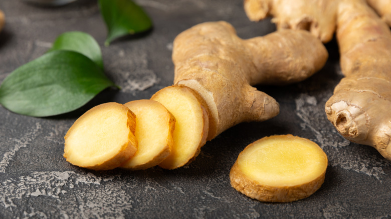 Chopped ginger root on a dark black board with leaves in the back