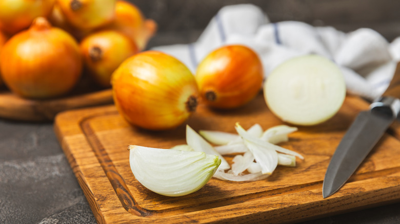 Cut onion on a cutting board with more unpeeled onions in the back