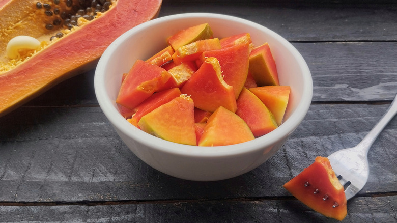 Bowl of fresh papaya cut in bowl with whole fruit in the back and one piece on a fork next to it