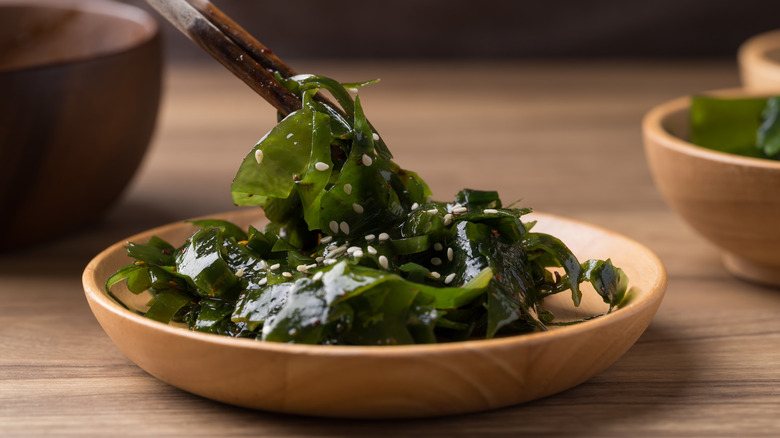 Using chopsticks to pull edible seaweed in a wooden bowl sprinkled with sesame seeds