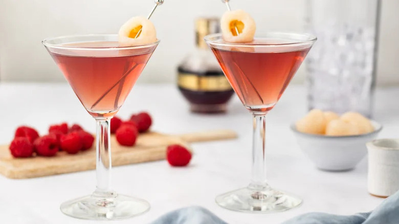 Two martini glasses with fruit background and lychee garnish.