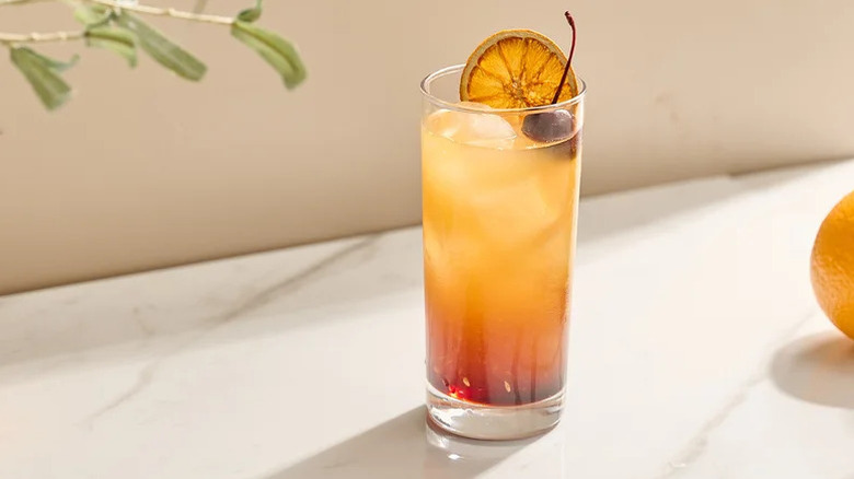 Collins glass, orange cocktail with garnish, on marble counter.