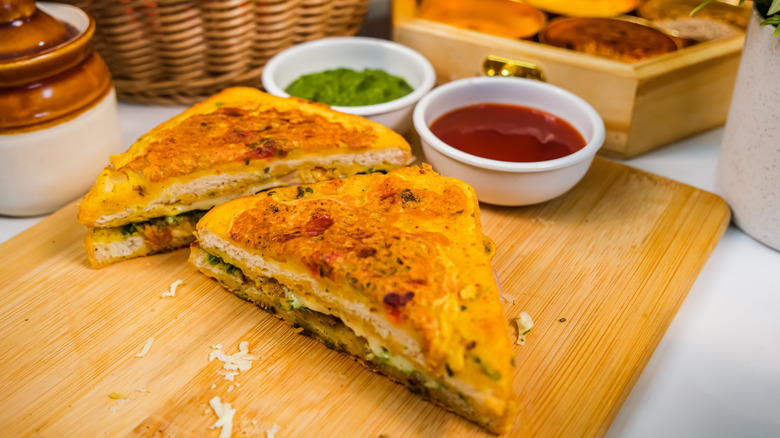 Bombay grilled cheese sandwich on wooden board with various dips