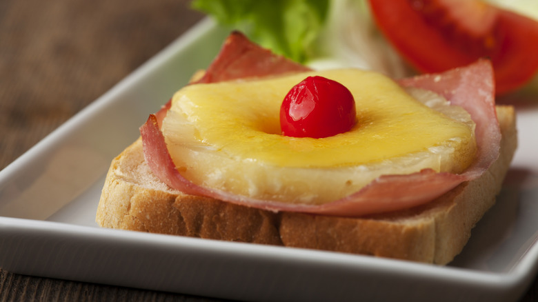 Plate of toast Hawaii topped with ham, pineapple, and a maraschino cherry
