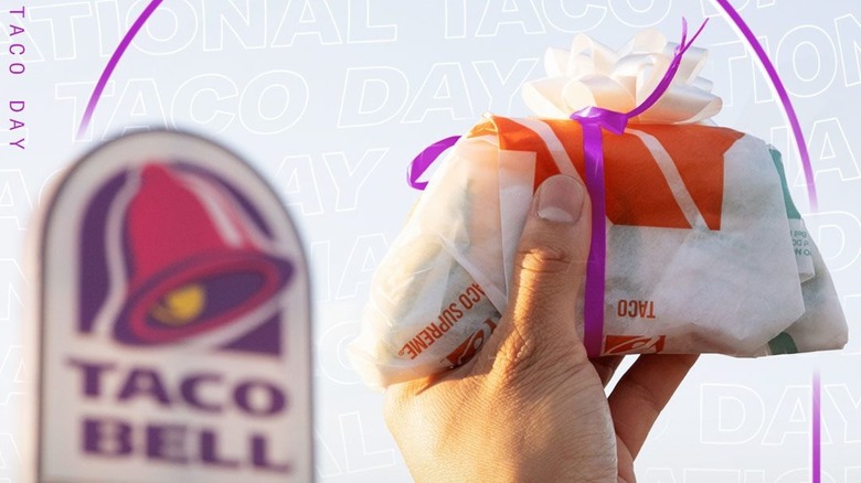 hand holding wrapped taco bell taco taco with taco bell sign in the background