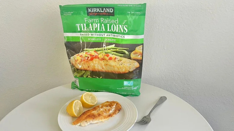 A package of Kirkland Signature Tilapia Loins on a table next to a cooked piece of fish