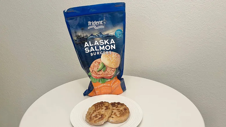 A package of Trident Seafoods Alaskan Salmon Burgers on a table with two burger patties on a plate