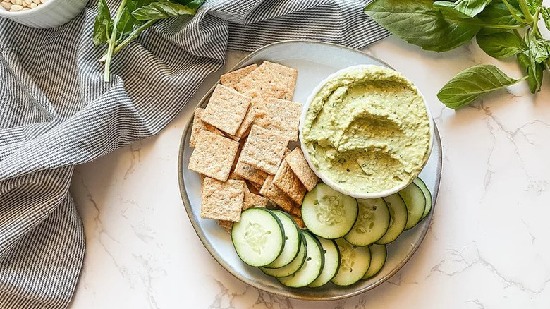 Homemade Pesto Hummus on plate with crackers and cucumbers