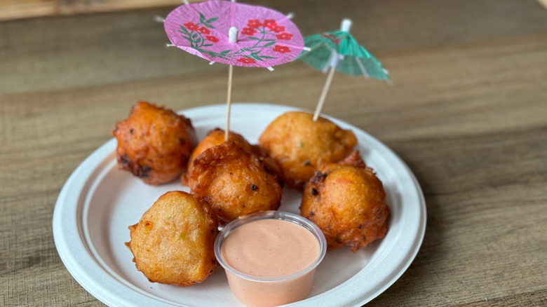 Conch fritters on off-white disposable plate with cup of sauce and little umbrellas