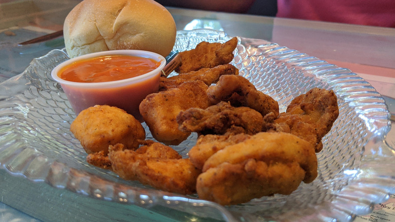Glass dish with fried gator bites, cup of sauce, and a bread roll