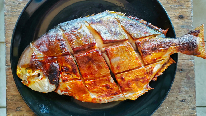 Top view of a whole grilled pompano fish served on black plate
