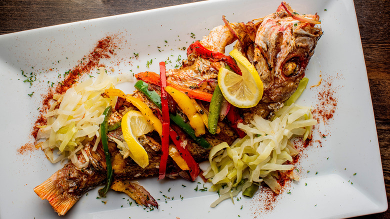 Grilled whole red snapper topped with julienned veggies and lemon slices served on white rectangular plate