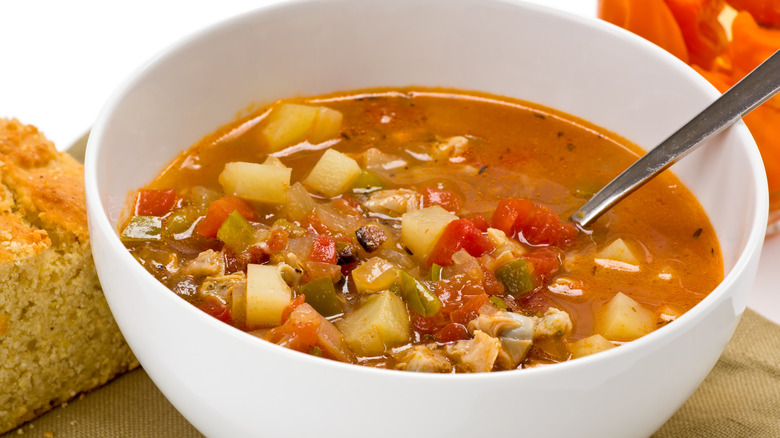 Small white bowl of tomato-based Minorcan clam chowder with calms and veggies with a spoon inside