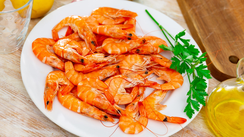 White plate filled with raw royal red shrimp with a sprig of herb