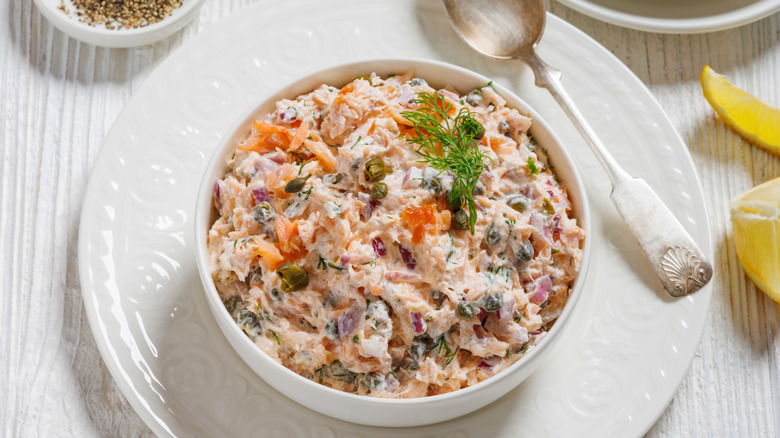 White bowl of salmon smoked fish dip garnished with herb sitting on white plate with spoon
