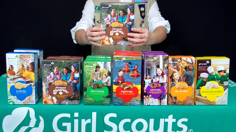 A Girl Scout standing beside several Girl Scout cookie flavors