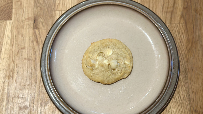 Overhead image of white chocolate macadamia nut cookie on a plate on a wooden counter
