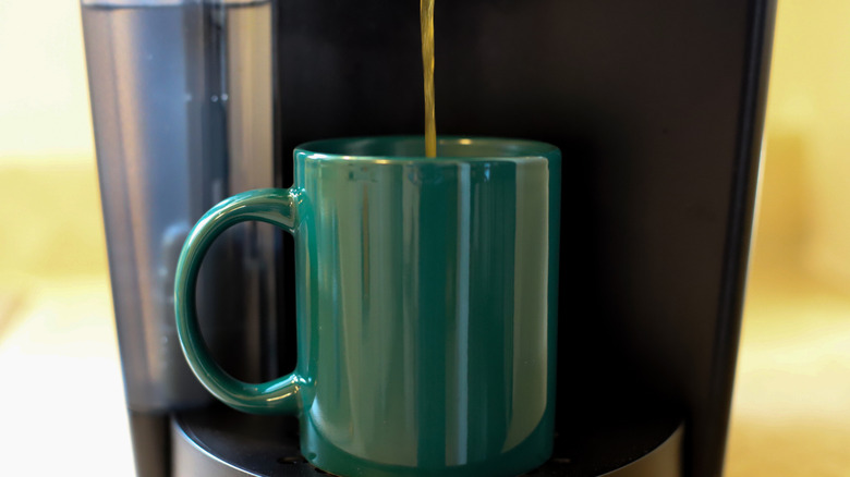 A close-up of a hunter green mug in a Keurig machine being filled with coffee