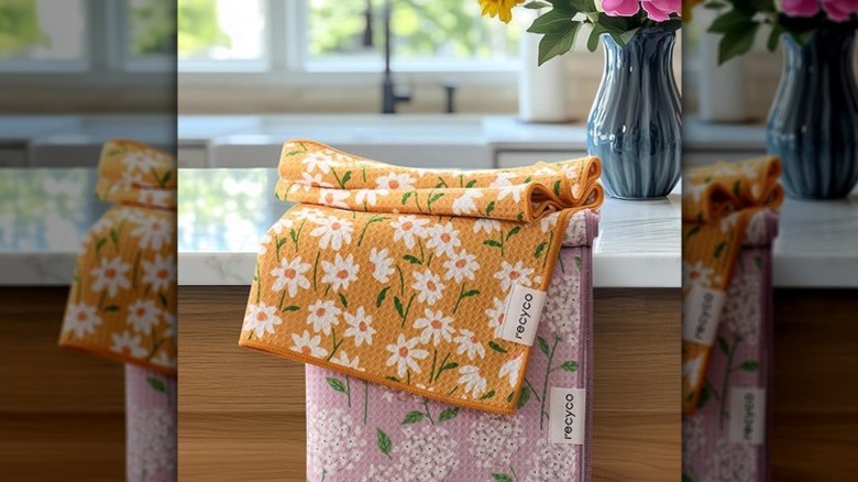 Two kitchen towels on counter with flower vase