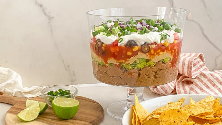 Vegan seven-layer dip in trifle dish with chips and cut limes
