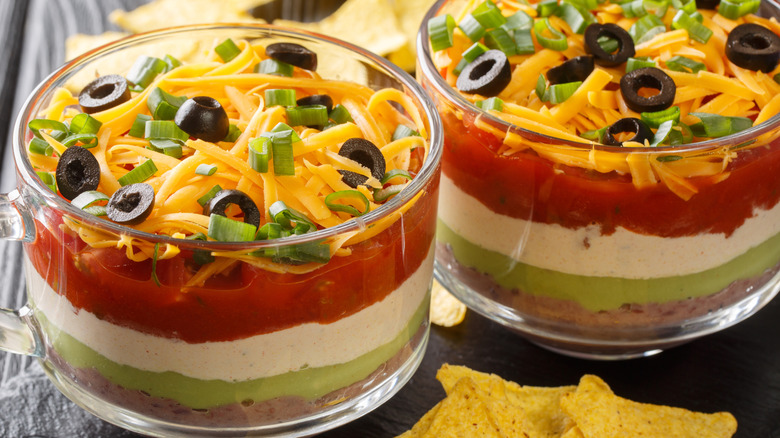 Two bowls of seven-layer dip with cheese and olives on top