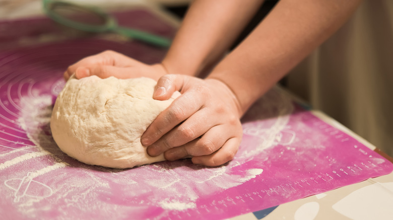 Hands kneading dough on pink silicone baking mat