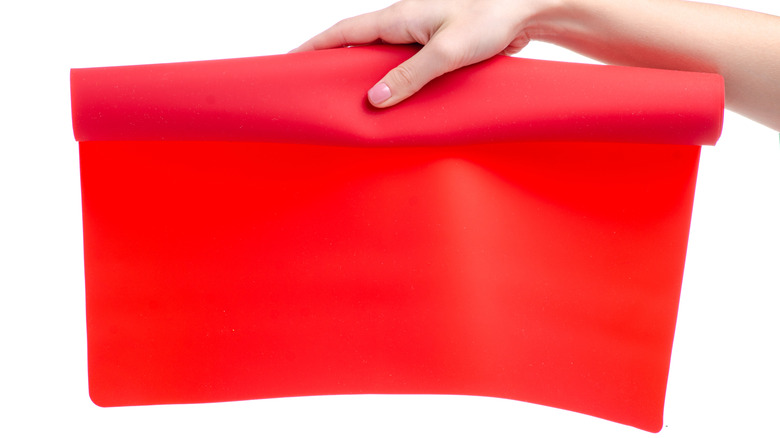 Hand holding silicone baking mat on white background